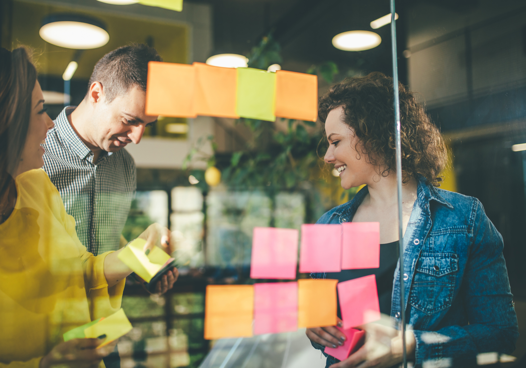 Personen stehen hinter einer mit Post-It beklebten Glaswand