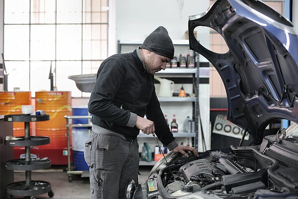 KFZ-Mechatroniker steht vor offener Motorhaube und repariert diese